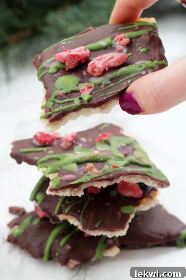 A stack of paleo Christmas Crack with a hand taking the top piece off, featuring red and green toppings.