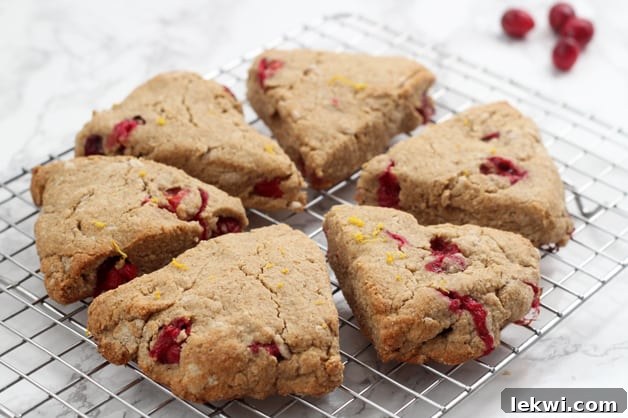 Two orange cranberry scones, drizzled with coconut butter and orange zest, on a white background.