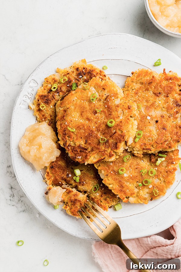 Fork on a plate with two sweet potato latkes, ready to be eaten.
