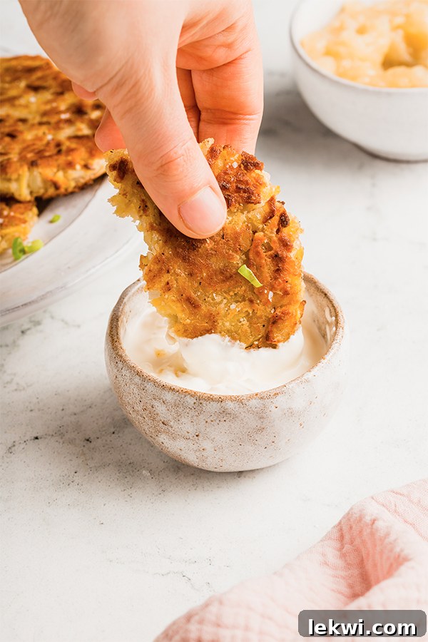 A person dipping a sweet potato latke into a creamy white sauce.
