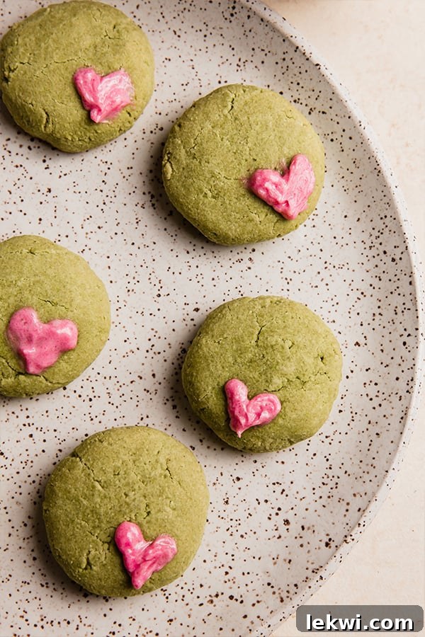 A second close-up shot of a plate of vibrant green Grinch cookies, each featuring a small red heart, presented beautifully for the holiday season.