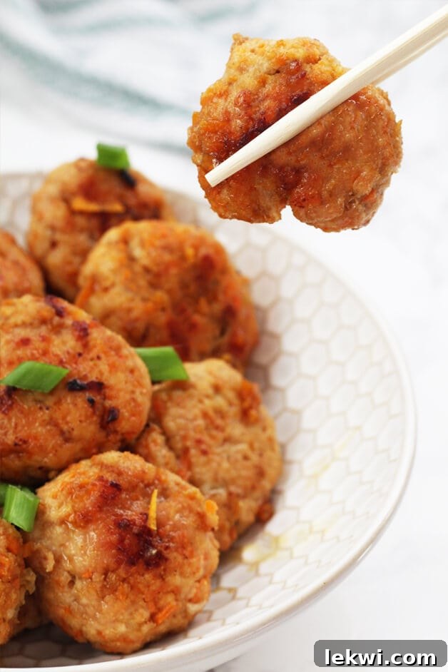 A close-up shot of several Paleo Whole30 AIP Orange Chicken Poppers in a serving bowl, coated in sauce.