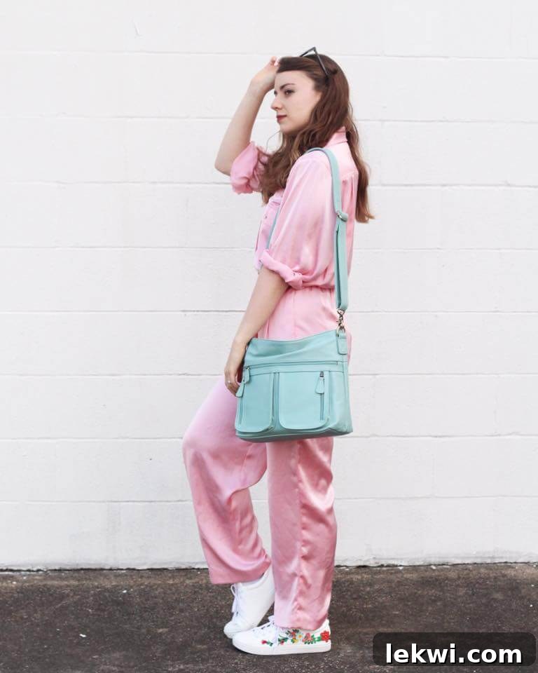 Michelle in a bright pink 80s jumpsuit, holding a blue purse, against a white concrete background.