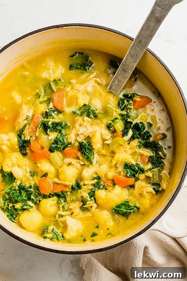 Spoon in a bowl of bright turmeric chicken soup.