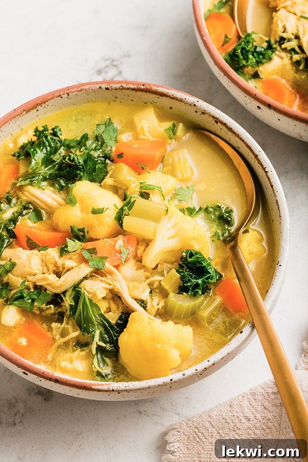 Spoon in a bowl of bright turmeric chicken soup.
