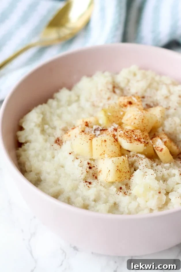 A vibrant pink bowl showcasing a serving of grain-free cauliflower 'oatmeal,' beautifully garnished with a sprinkle of cinnamon and fresh apple slices. The warm, inviting presentation highlights the delicious and healthy nature of this breakfast alternative.
