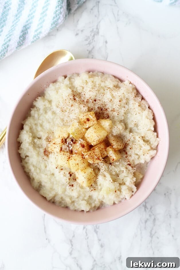 An inviting close-up shot of Grain-Free Cauliflower "Oatmeal" in a beautifully styled bowl. The texture of the cauliflower is subtly visible, and the dish is artfully arranged with toppings like cinnamon and fresh apple pieces, making it appear both wholesome and appetizing. This image reinforces the idea that healthy, grain-free alternatives can be just as appealing and satisfying as their traditional counterparts, making it suitable for Paleo, AIP, and Whole30 lifestyles.