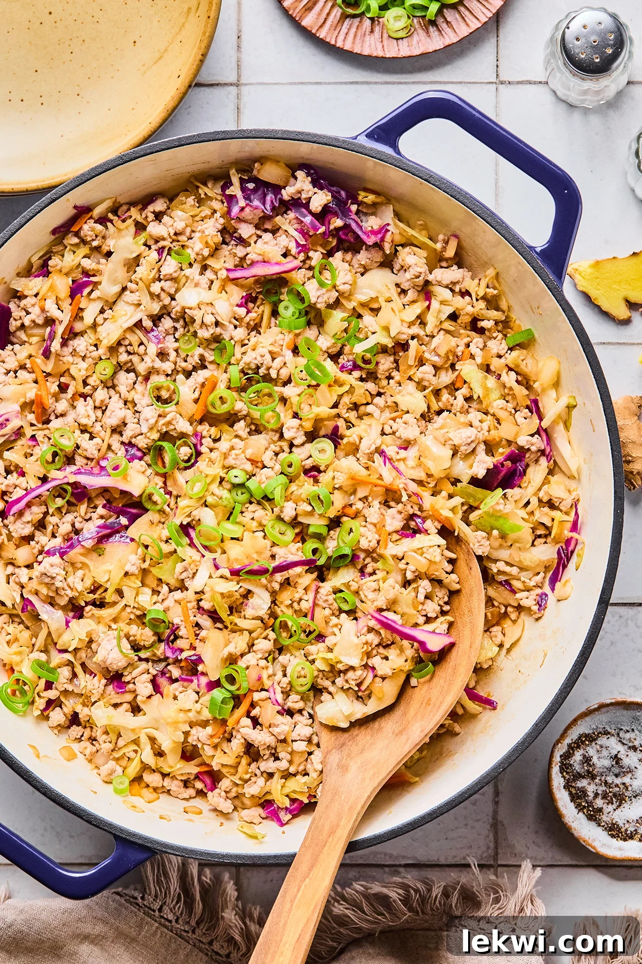 A Dutch oven filled with egg roll in a bowl after being cooked with a wooden serving spoon in it.