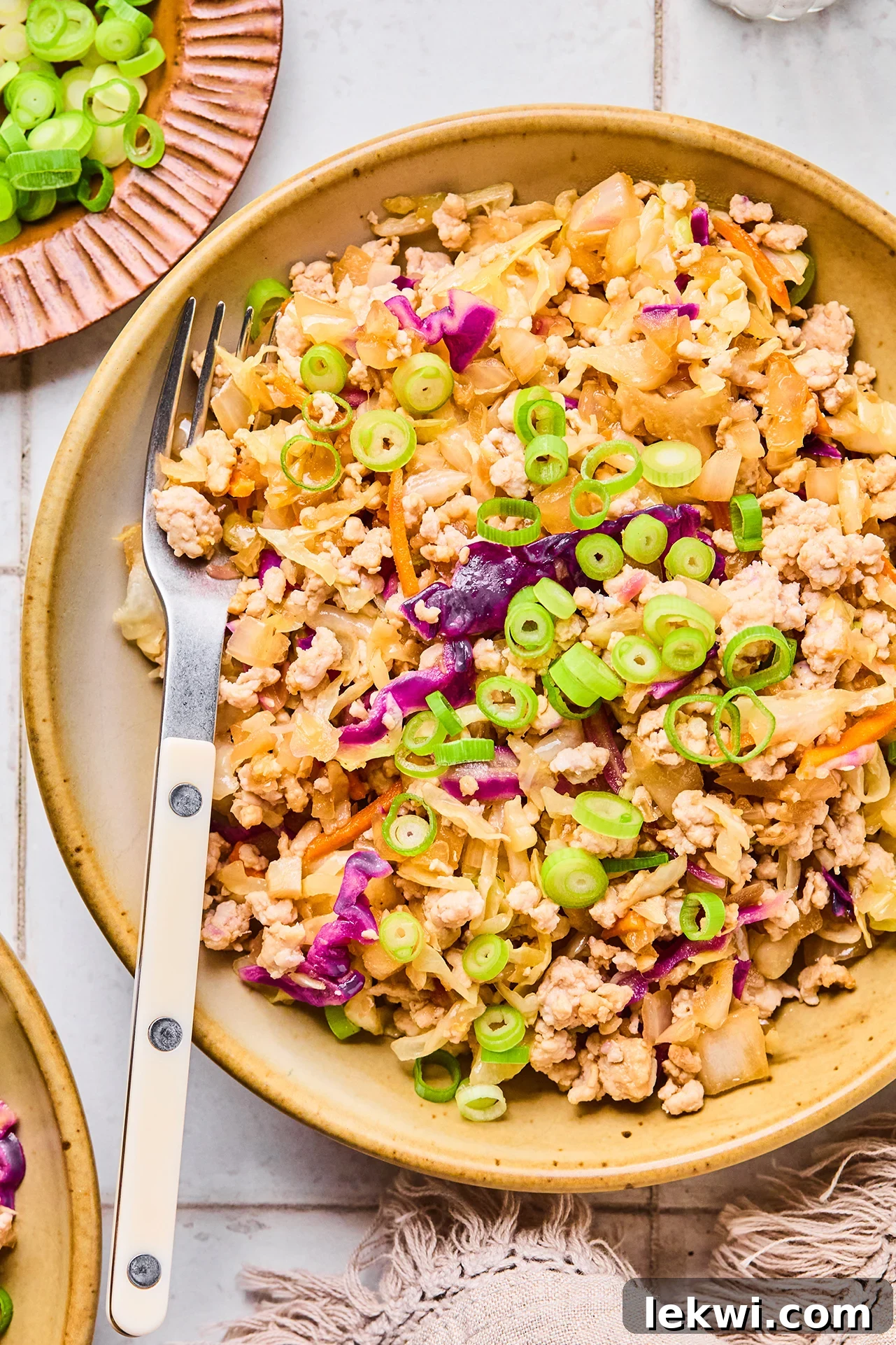 Egg roll in a bowl in a white dish with a fork topped with green onion.