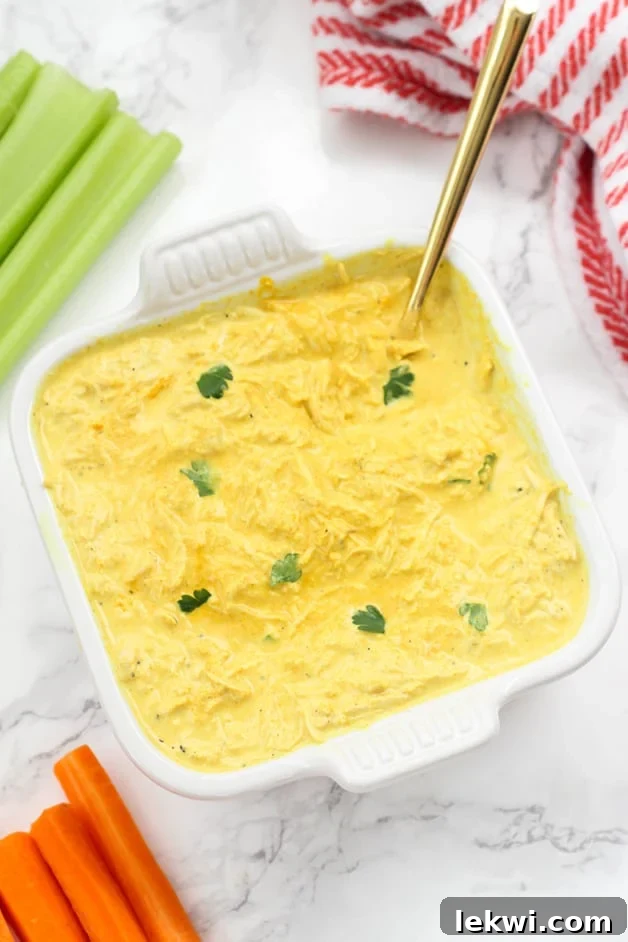A white ceramic dish filled with buffalo chicken dip and a spoon in it and some celery next to it.