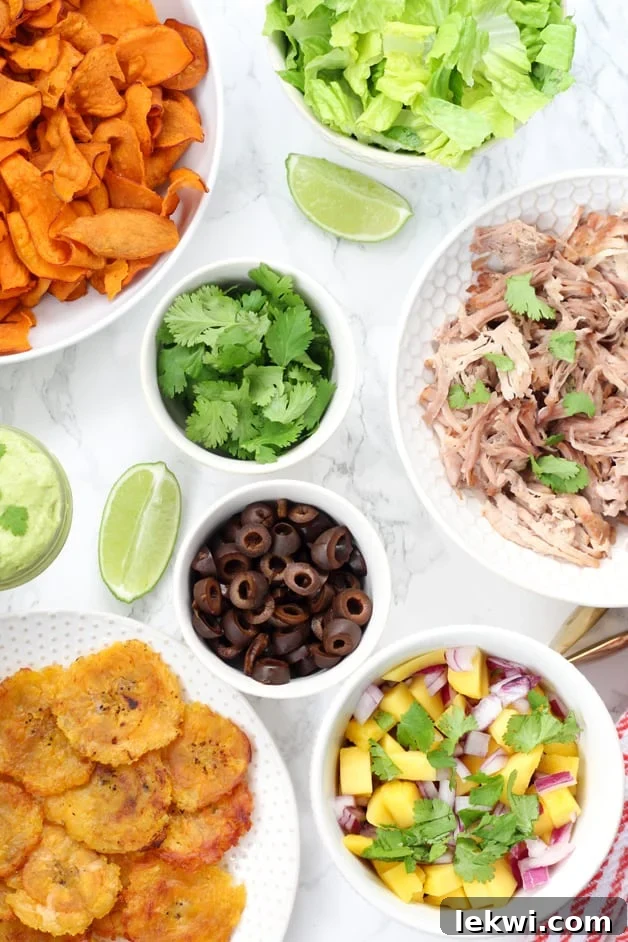 White bowls of ingredients including plantains, carnitas, olives, salsa, cilantro, and lime to make nachos, ready for a Paleo Nacho Bar