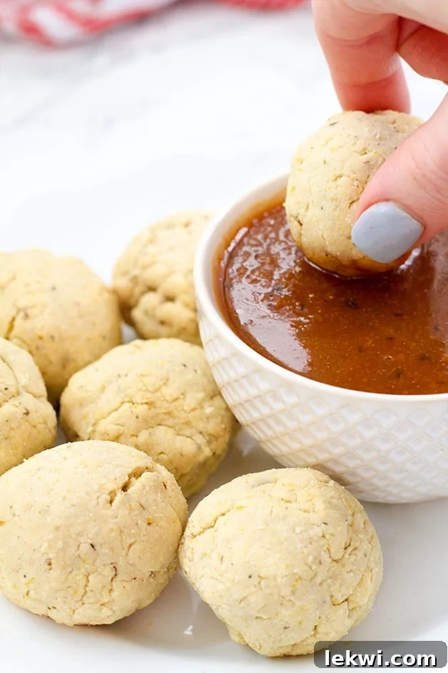 A hand dipping a pizza bite into red dipping sauce with other pizza bites next to the dipping sauce.
