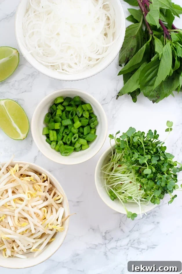 Bowls on a counter with sprouts, green onions, bean sprouts, rice noodles, and lime wedges ready to make pho.