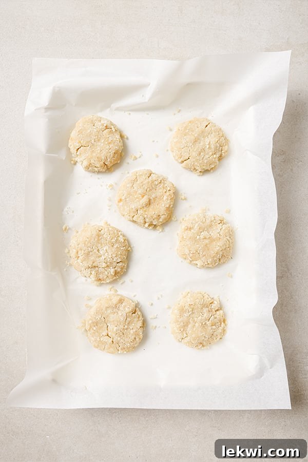Seven shaped cauliflower veggie nugget patties arranged neatly on a parchment-lined baking sheet, prepared for baking.