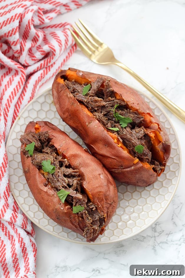 Two sweet potatoes on a plate stuffed with bbq beef and topped with fresh cilantro. A close-up showing the texture of the filling.