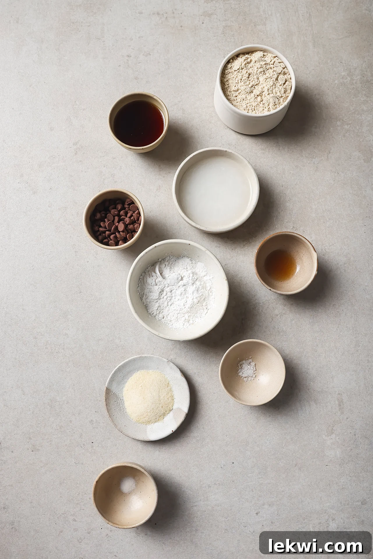 Individual bowls holding tigernut flour, tapioca starch, maple syrup, coconut oil, gelatin, and chocolate chips, ready for baking.
