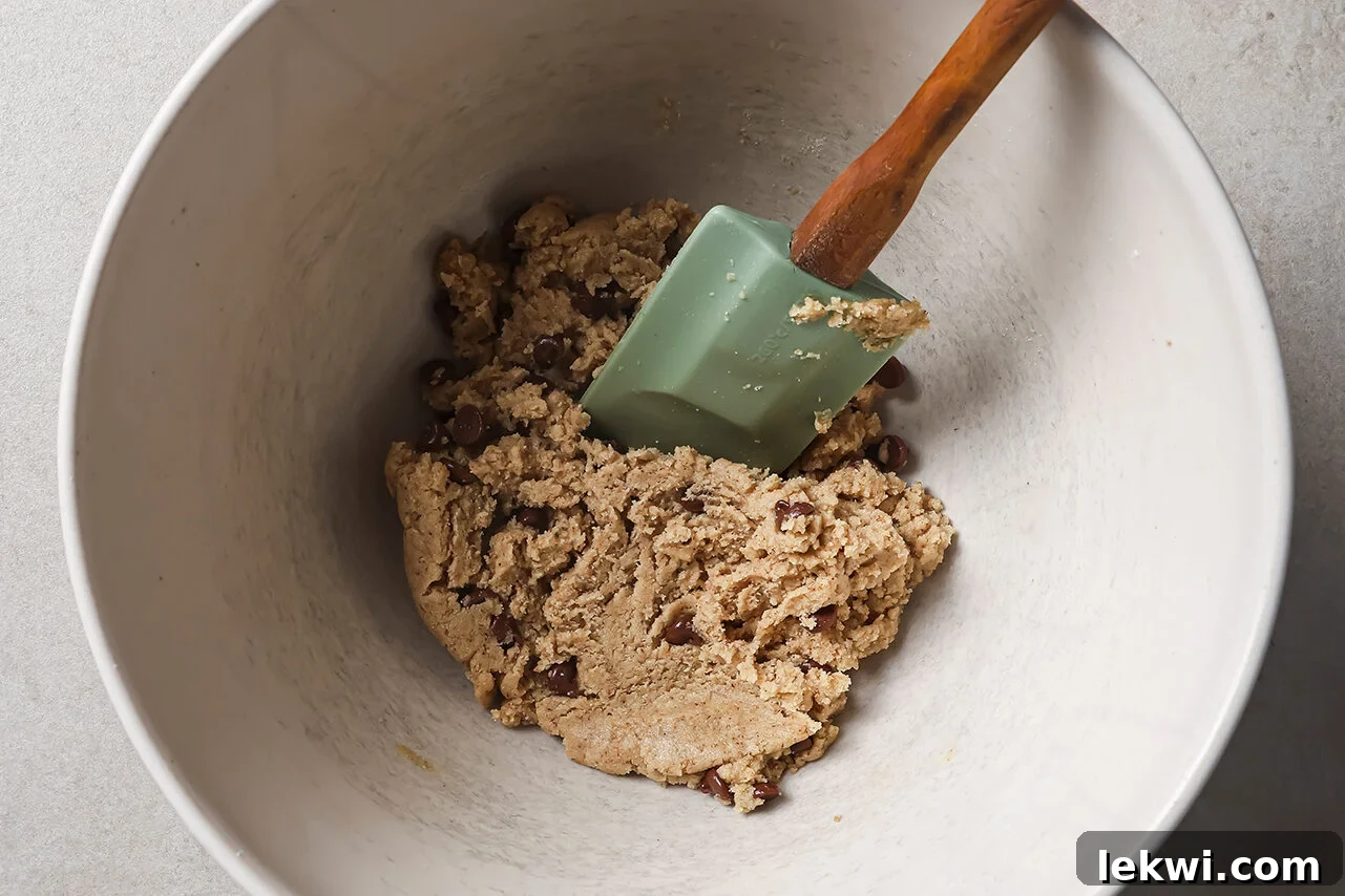 Wet ingredients: vanilla, maple syrup, and coconut oil being added to the dry mixture, with chocolate chips ready to be folded in.