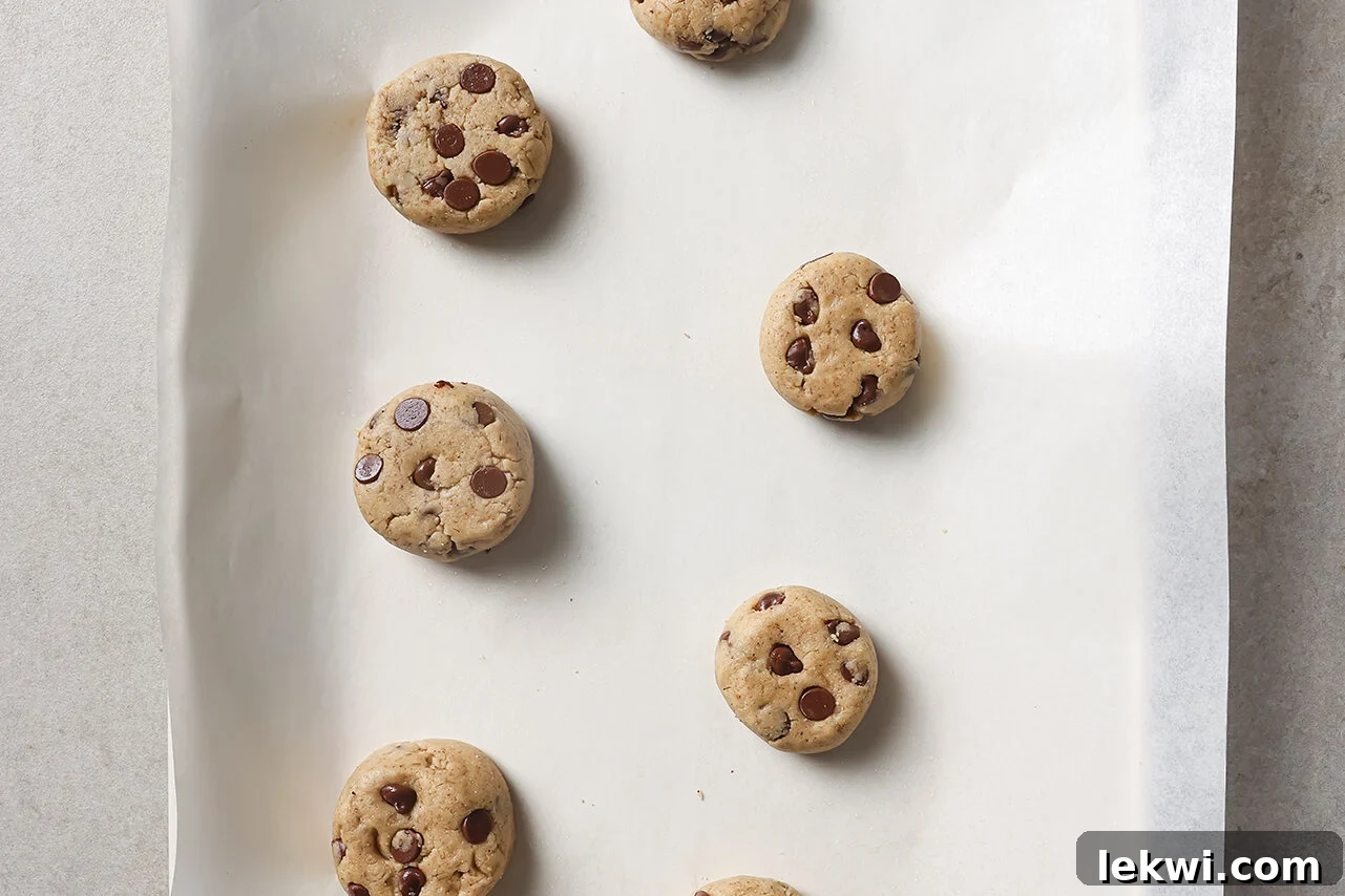 Cookie dough balls being formed and placed on a parchment-lined baking sheet, spaced apart.