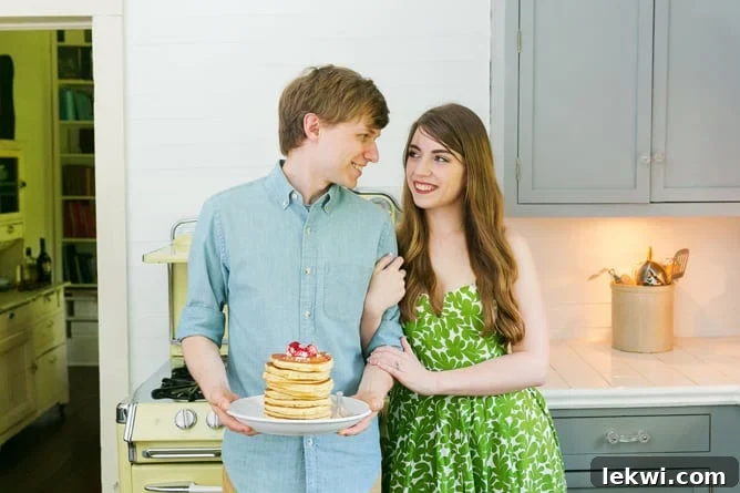 Michelle with her arm around Daniel who is holding a stack of fresh pancakes in a kitchen.