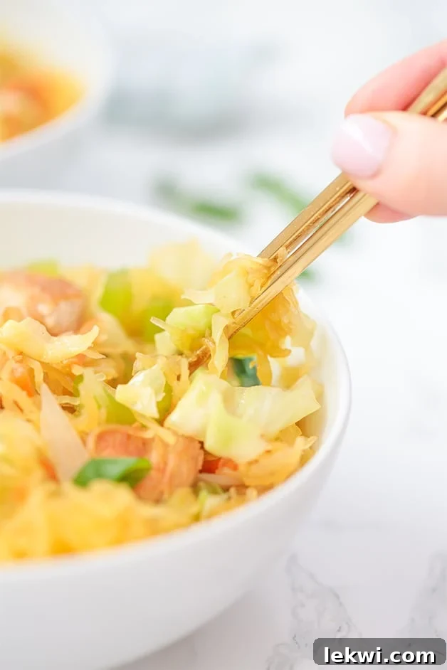 A white bowl filled with chow mein and a hand with gold chop sticks in it.
