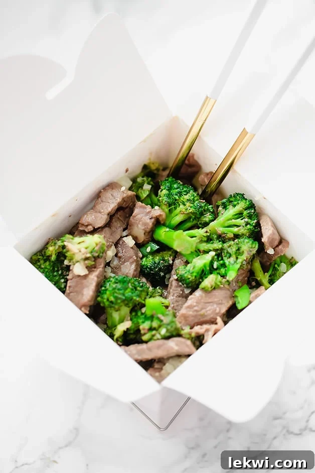A white takeout container filled with beef and broccoli and chop sticks in it.