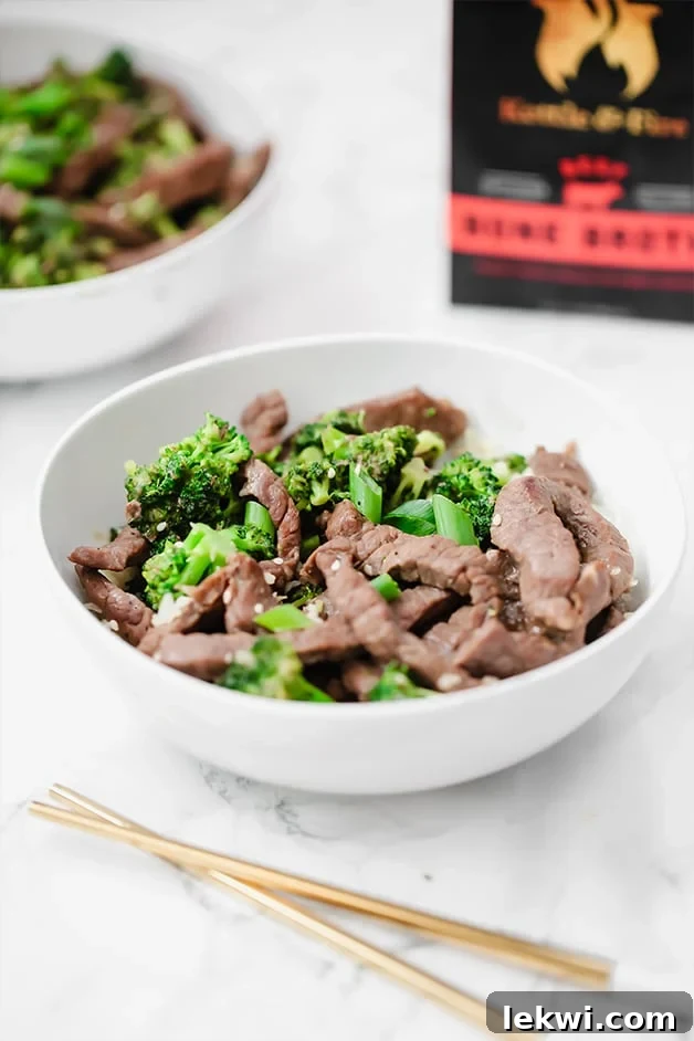 A white bowl with beef and broccoli stir fry in it and chop sticks next to it.