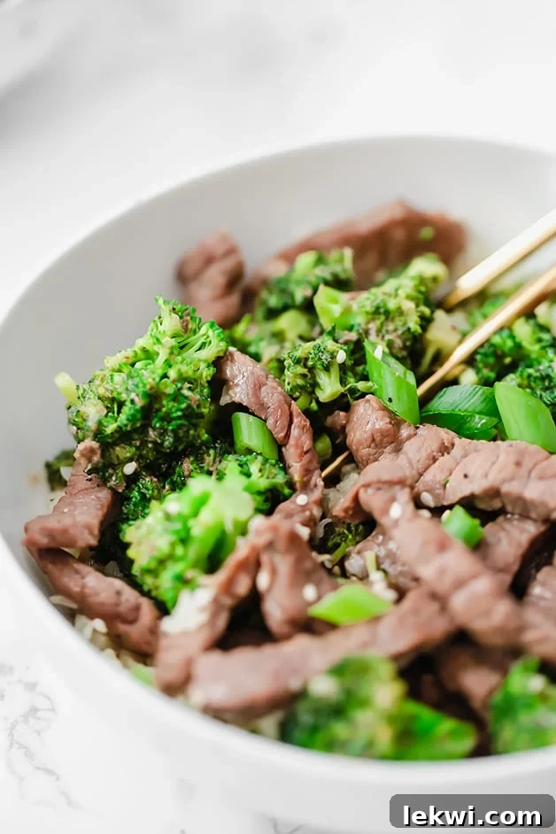 A white bowl with beef and broccoli stir fry in it and chop sticks in it.