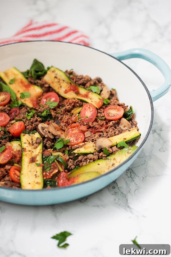 A blue pan filled with zucchini, tomato, ground beef, and herbs.