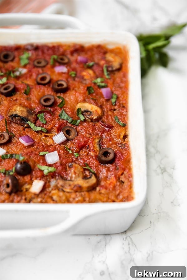 A white baking dish filled with spaghetti squash pizza casserole topped with olives, mushrooms, and onions.