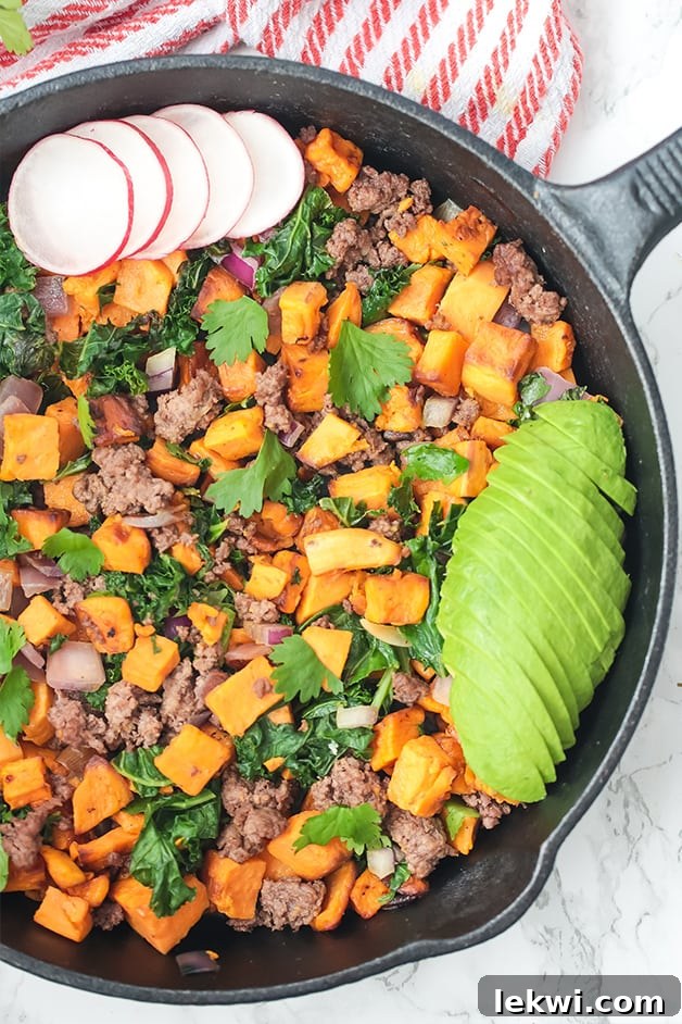 A black skillet filled with butternut squash, ground beef, avocado, radish and more to make a taco skillet.