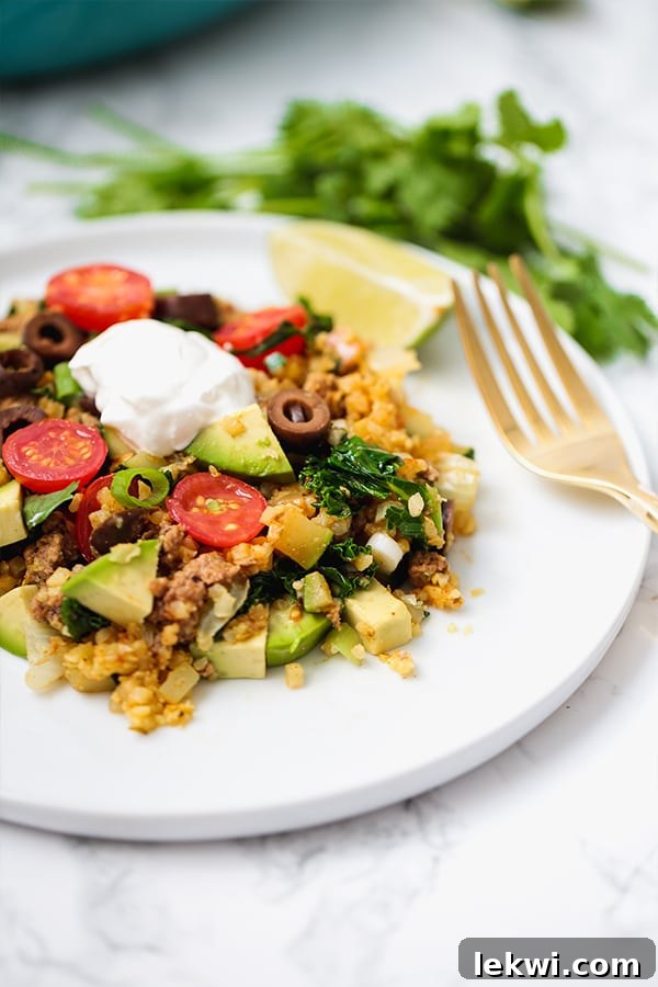 A white plate with a serving of taco skillet on it and a fork next to it.