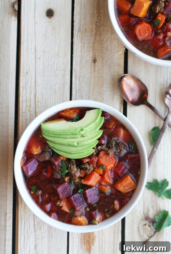 A white owl filled with AIP chili and topped with avocado sitting on a wooden table.
