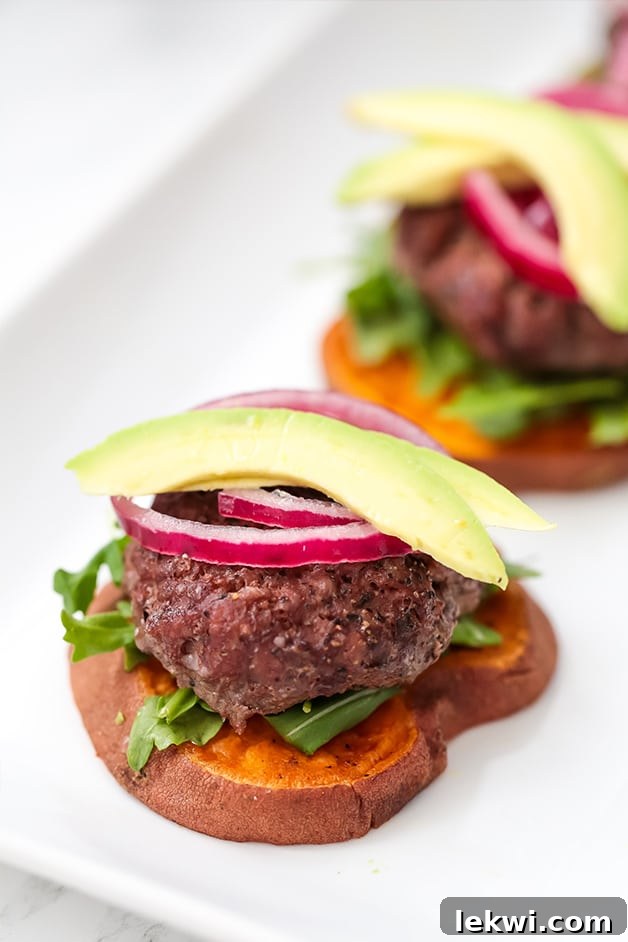 A slider on a sweet potato bun topped with red onion and avocado with another in the background.