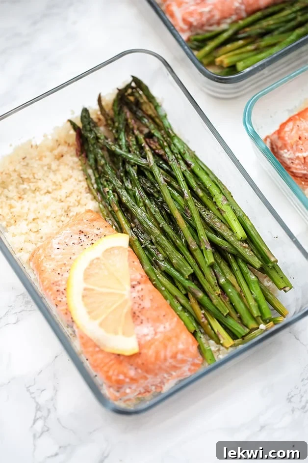 A glass meal prep container filled with roasted asparagus, salmon, and cauliflower rice, ready for a healthy meal.