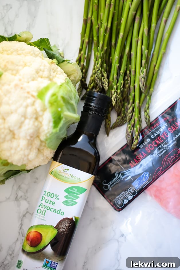 Fresh ingredients laid out on a kitchen counter, including avocado oil, a head of cauliflower, a bunch of asparagus, and salmon fillets, all from ALDI.
