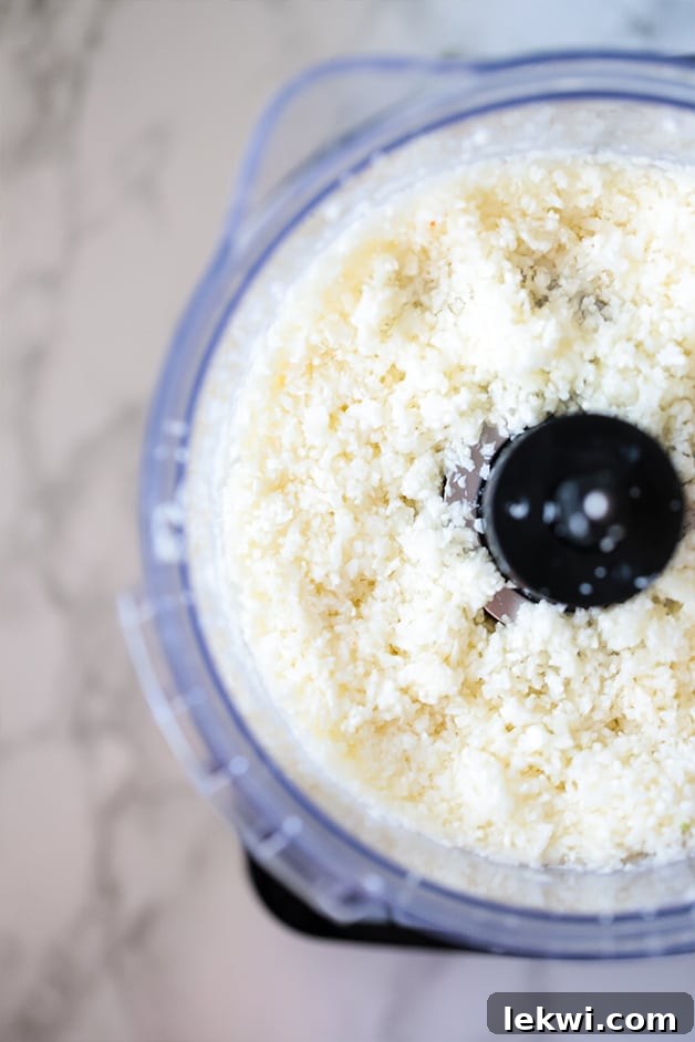 An open food processor filled with freshly riced cauliflower, ready for cooking.