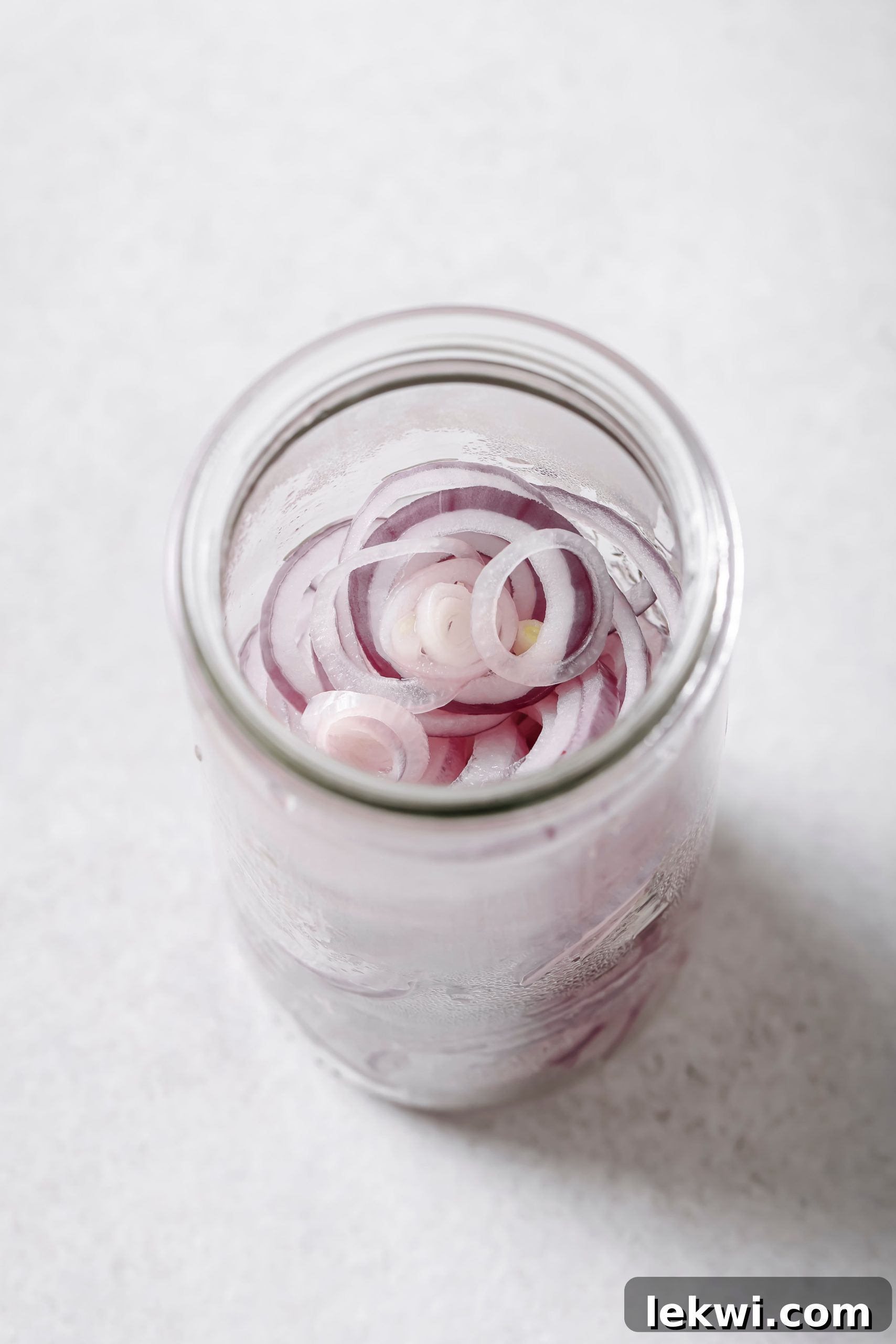Softened red onion slices in a fine mesh strainer after being blanched.