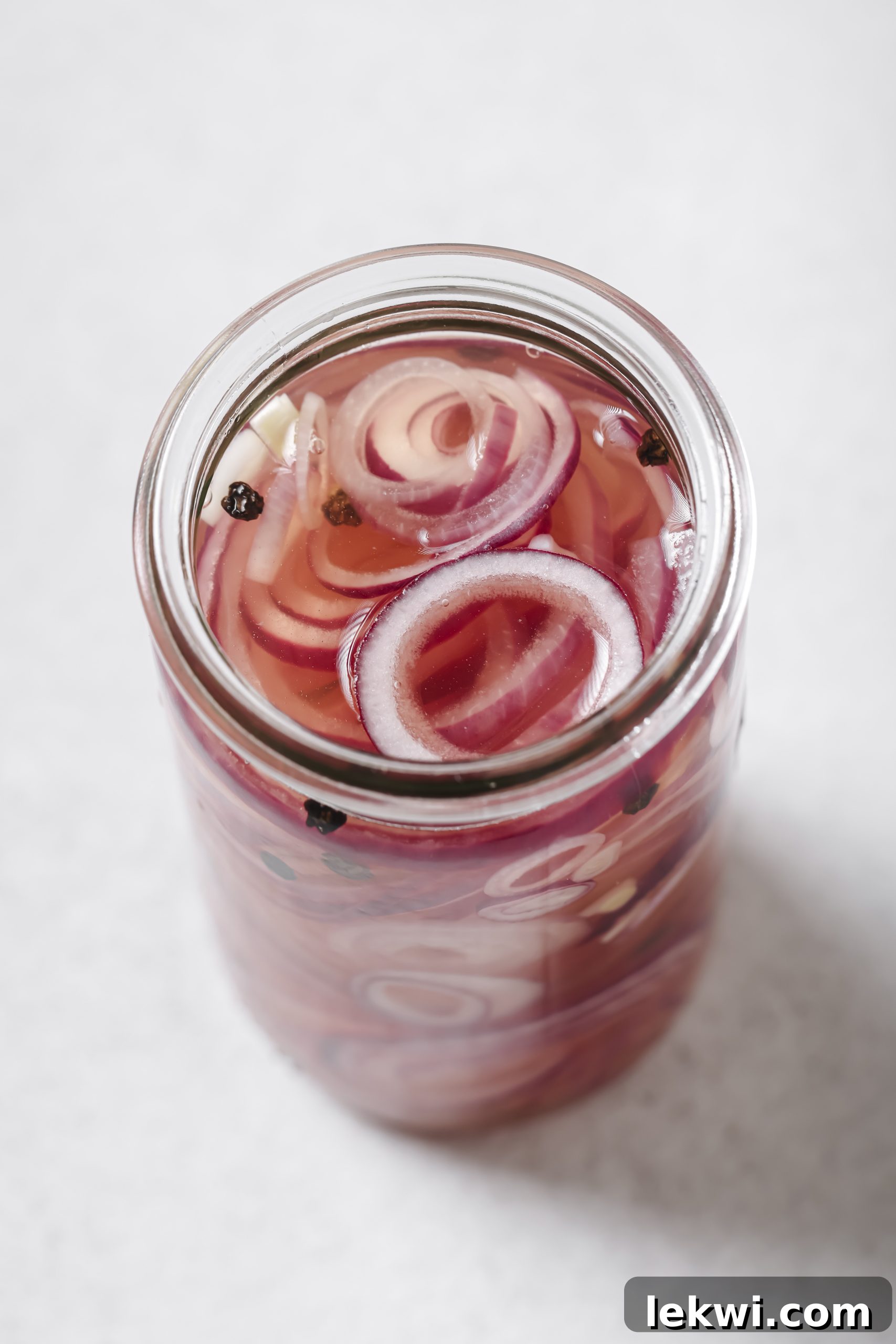 Red onion slices submerged in apple cider vinegar in a jar, ready for pickling.