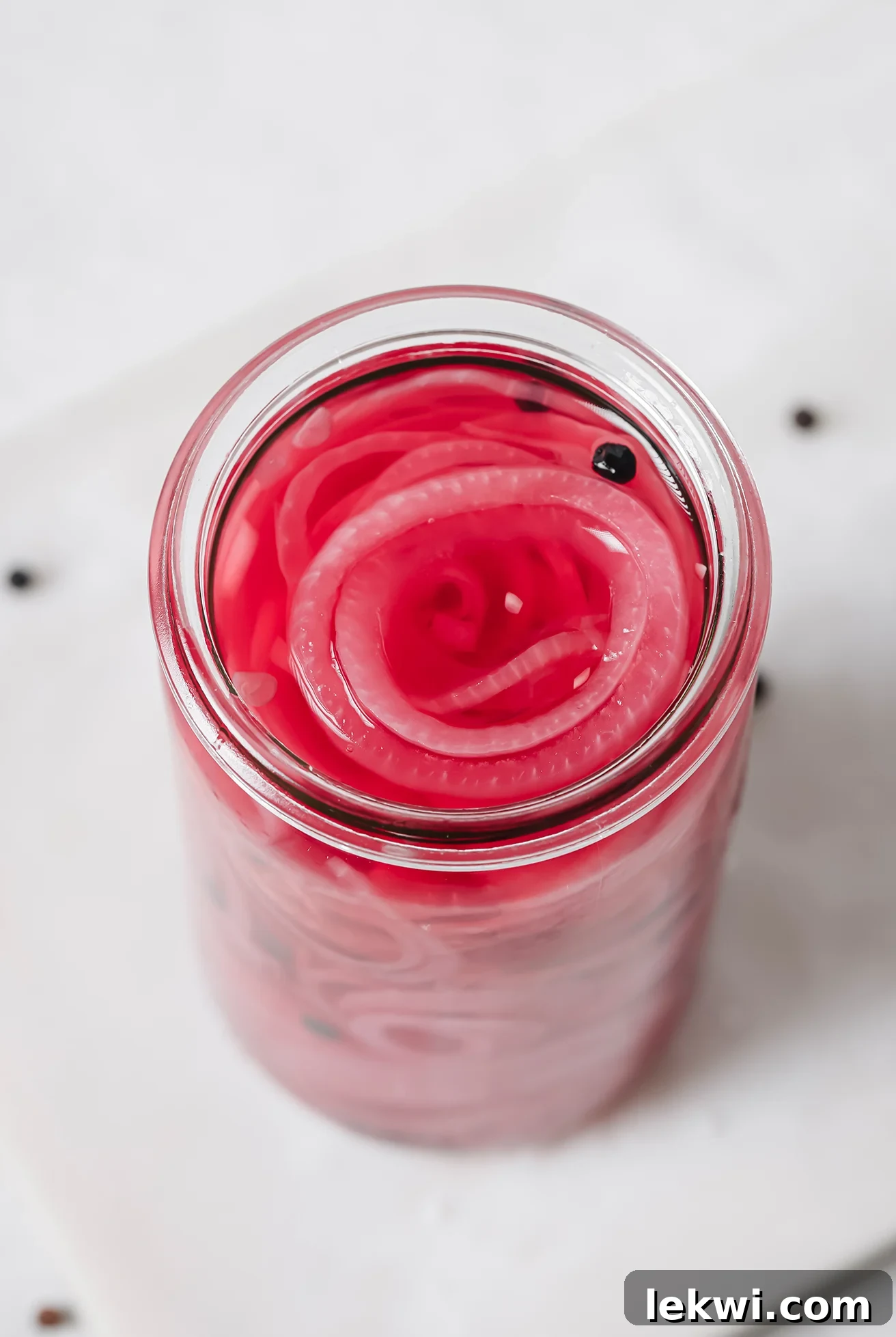 Close-up of apple cider vinegar pickled onions in a glass jar, showing their bright pink color.
