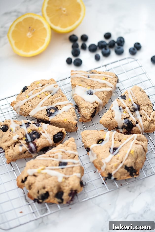 Six lemon blueberry scones on a metal cooling rack with fresh blueberries and lemon slices nearby.