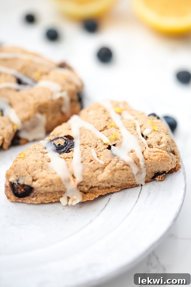 A white plate showcasing two exquisite lemon blueberry scones, delicately topped with a light frosting, ready to be enjoyed.