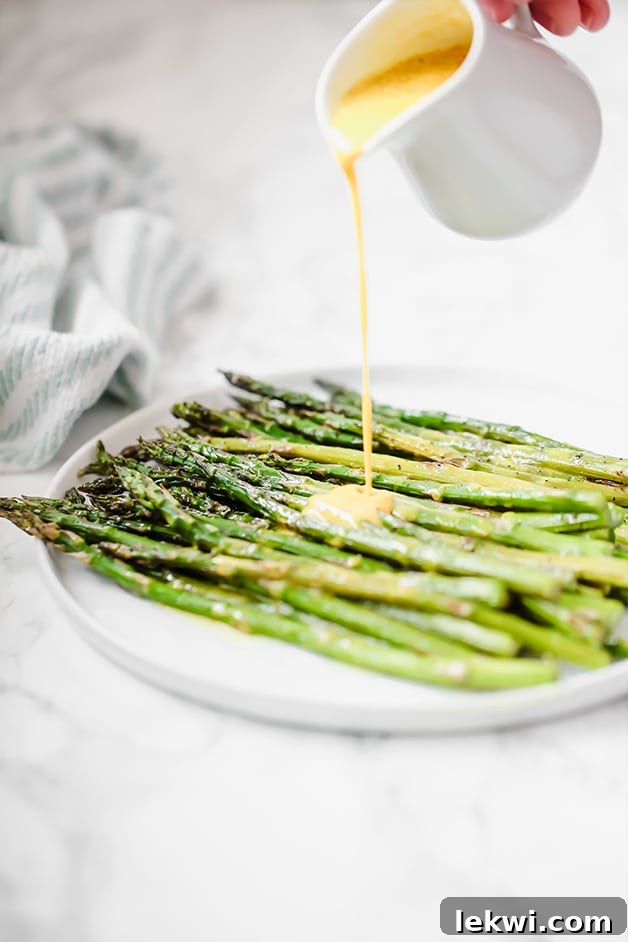 A white plate filled with roasted asparagus with a sauce drizzling over it.