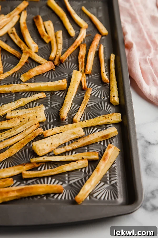 Parsnip fries baking on a sheet pan, turning golden brown and crispy.