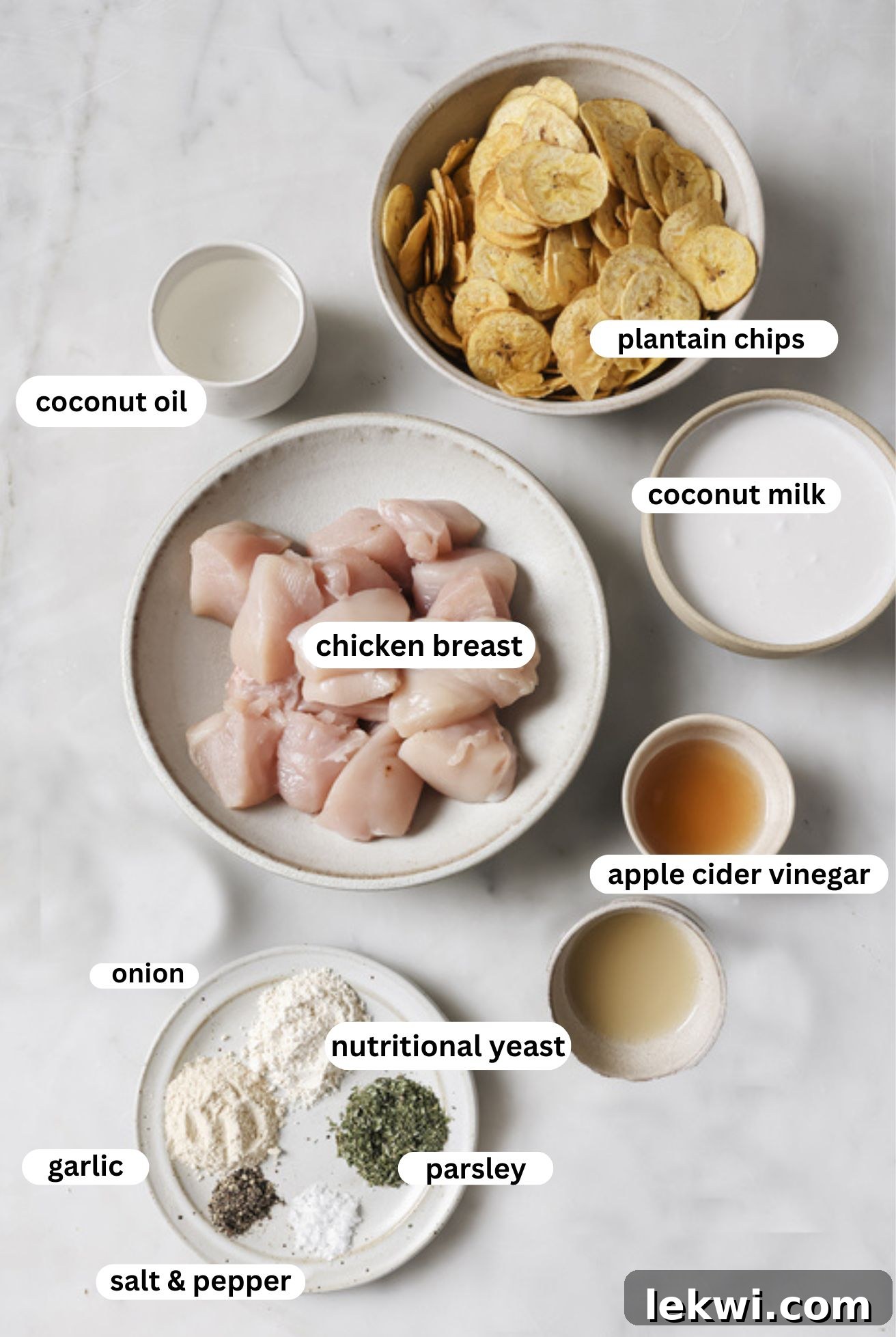 Labeled bowls containing the key ingredients for crispy chicken nuggets: chicken breast, plantain chips, coconut milk, apple cider vinegar, coconut oil, and a blend of herbs and spices.