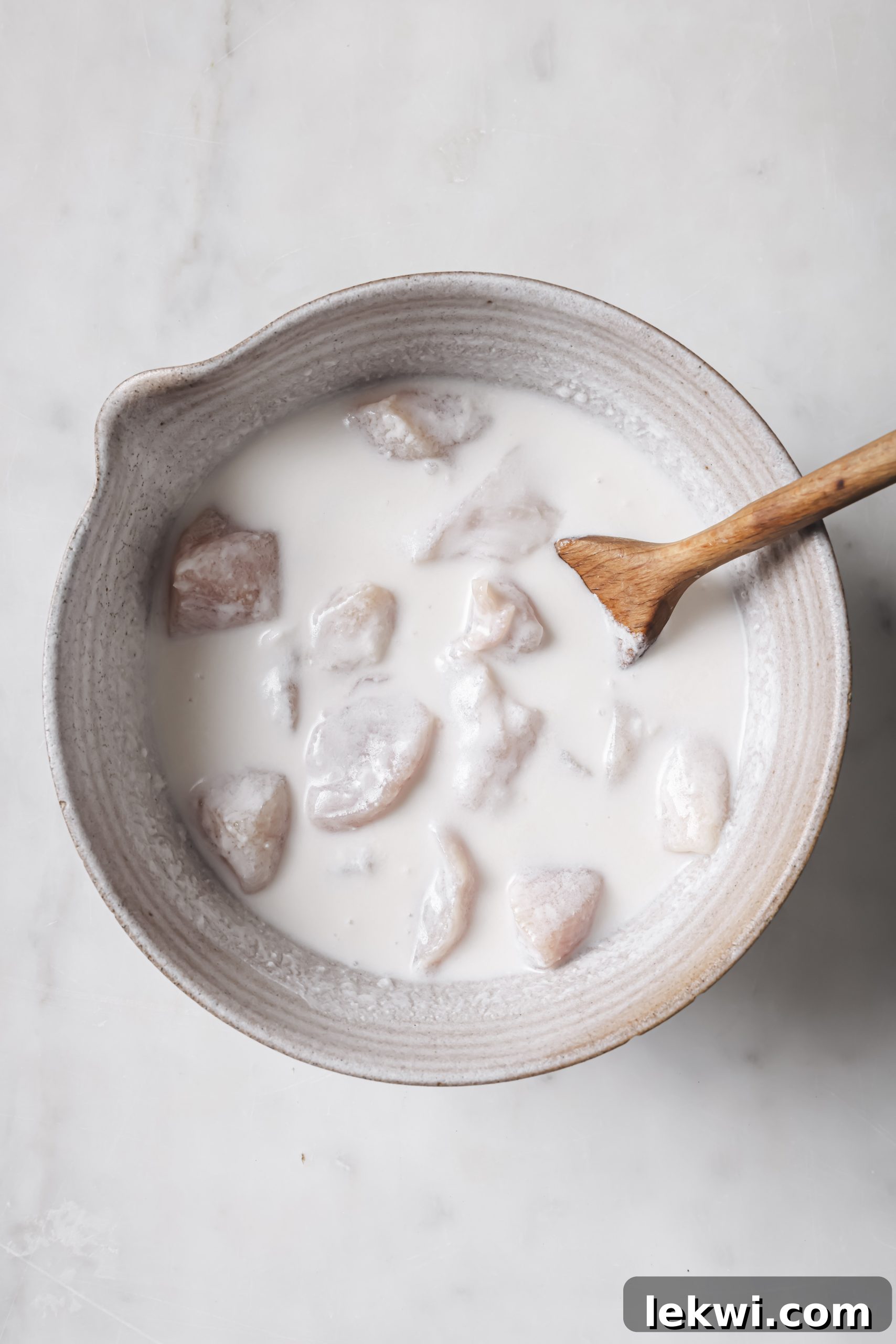 Chicken breast cubes marinating in a creamy coconut milk and apple cider vinegar mixture, absorbing flavors for tender nuggets.