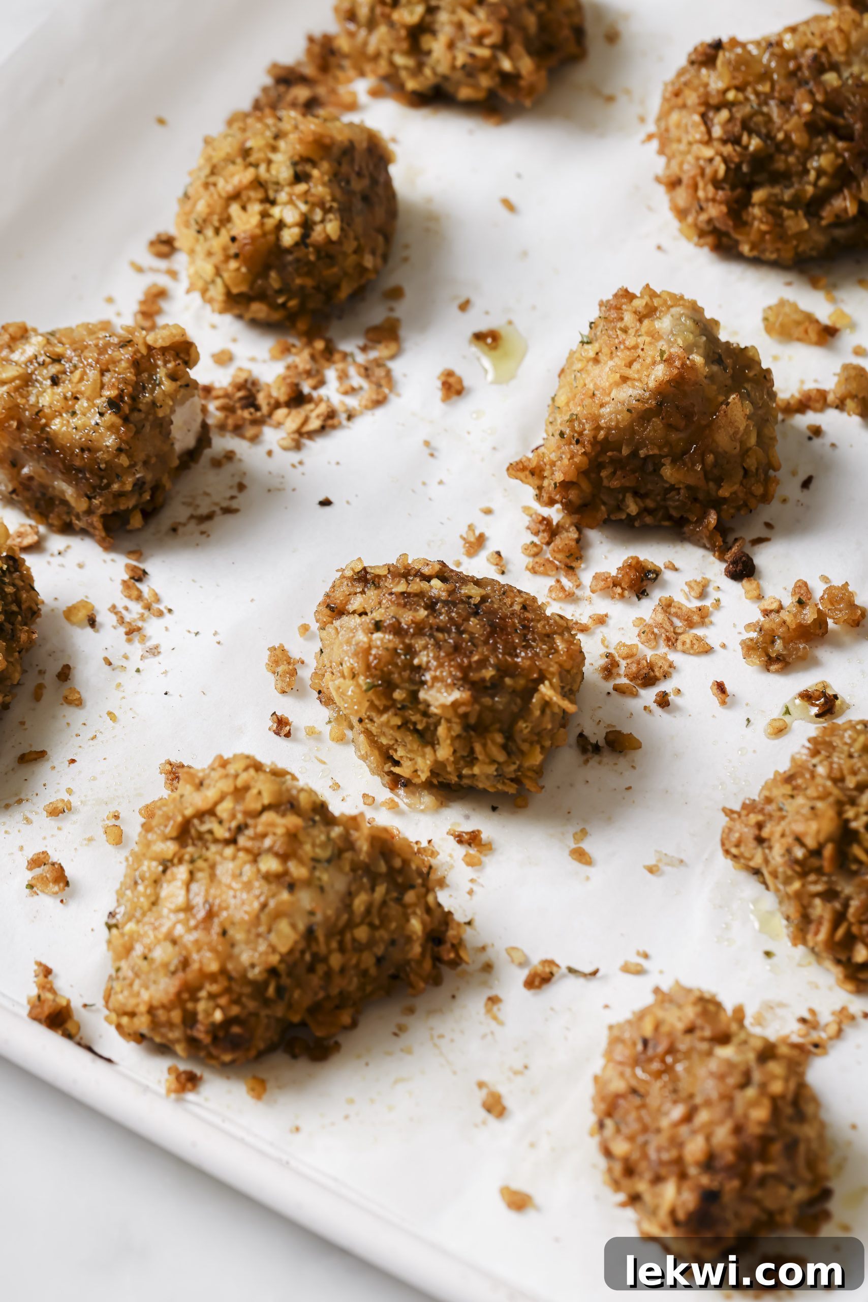A close-up shot of baked crispy chicken nuggets on a parchment-lined baking sheet, golden brown and ready to be served.