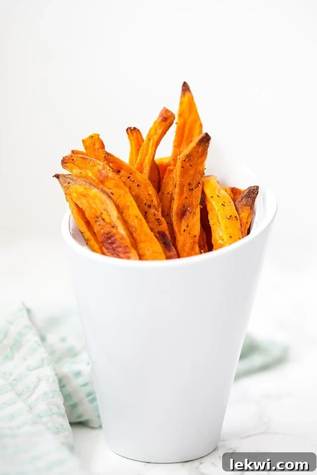 A white cup overflowing with golden, crispy baked sweet potato fries, perfect for a healthy snack or side dish.