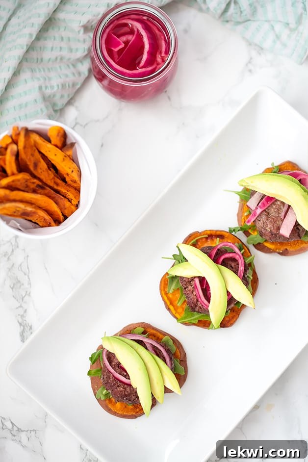 A white plate with three sliders on sweet potato buns with a bowl of sweet potato fries next to it, creating a complete and healthy meal.