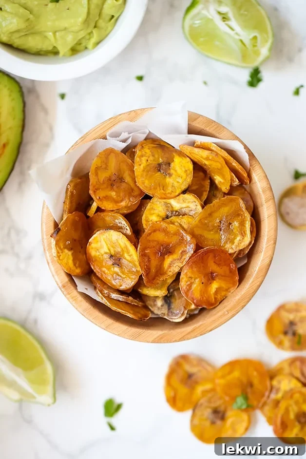 A wooden bowl filled with golden-brown, crispy baked plantain chips, perfectly seasoned.