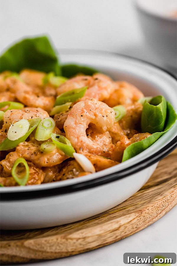 A white bowl filled with bang bang shrimp on a bed of lettuce topped with green onions, showcasing a delicious and healthy meal option.